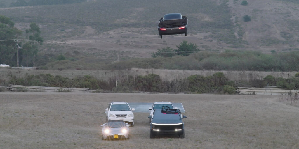 Tesla Roadster springt bei einer Vorführung über mehrere Fahrzeuge und befindet sich in der Luft.