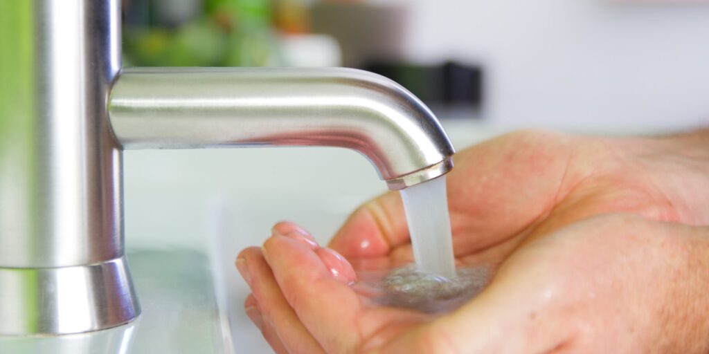 Wasser läuft aus dem Hahn in eine Hand