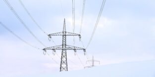Hochspannungsmasten mit Freileitungen in einer schneebedeckten Landschaft unter bewölktem Himmel.
