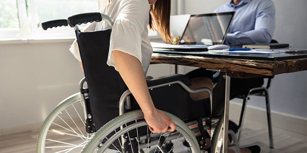 Frau mit steht mit Rollstuhl an einem Schreibtisch