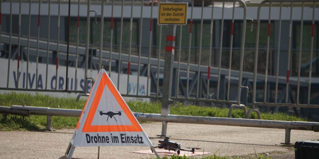 Auf dem Startplatz einer kleinen Drohne am Rhein ist ein Warnschild mit der Aufschrift "Drohne im Einsatz" zu sehen.