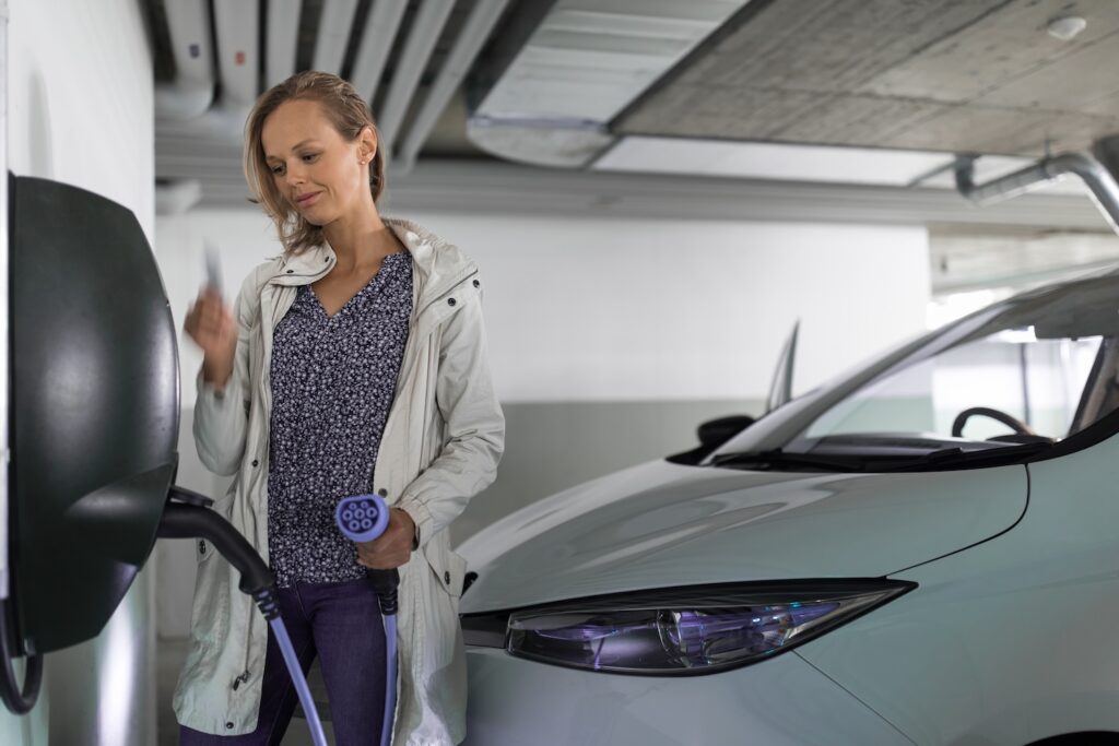 Frau steht mit einer Ladekarte in einer Tiefgarage vor einer Ladebox, das Kabel ist bereits mit dem Auto verbunden.