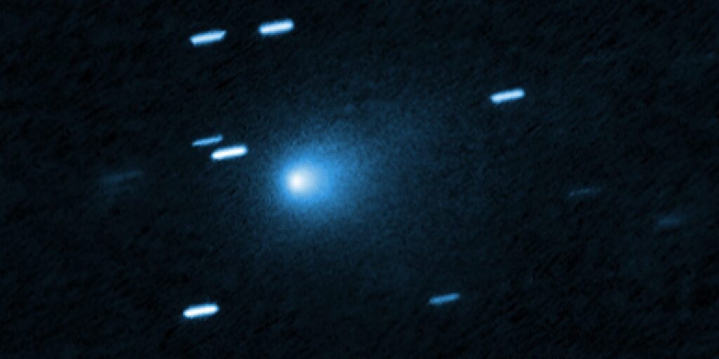 Hubble-Aufnahme von 3I/ATLAS mit bläulicher, tropfenförmiger Staubhülle und strichförmig abgebildeten Hintergrundsternen.