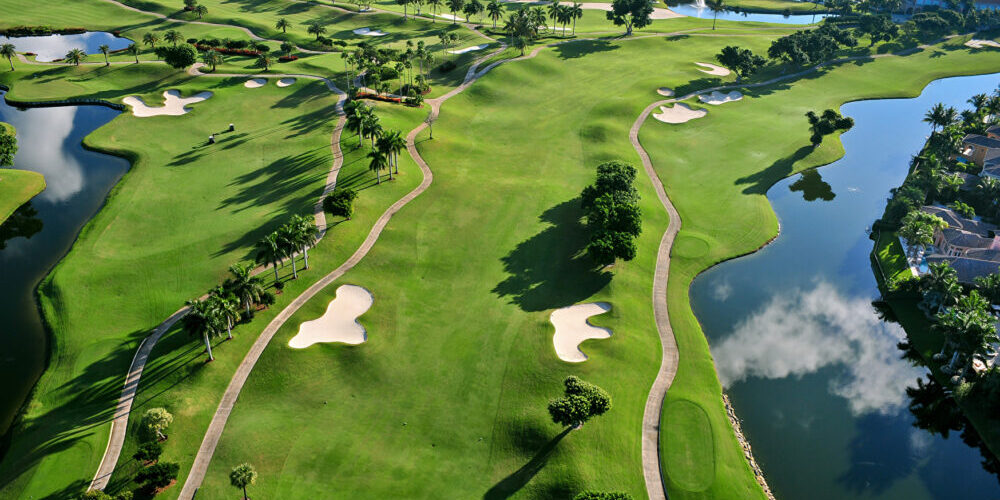 Blick von oben auf einen Golfplatz. Das satte Grün des Rasens wird durchbrochen von kleinen Sandlöchern und umrahmt von kleinen Seen.