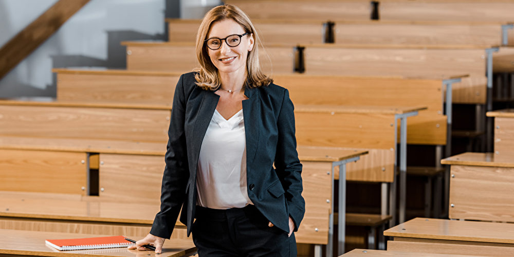 Frau in dunklem Anzug und Brille in einem Hörsaal