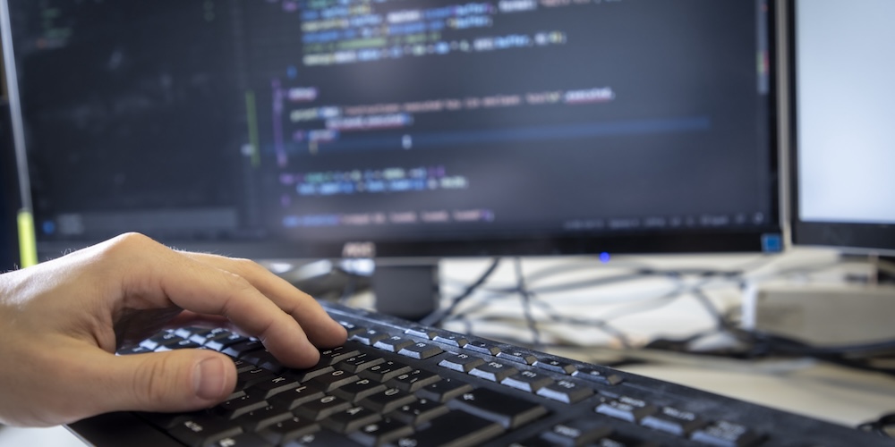 Hand auf Computertastatur mit Monitor im Hintergrund