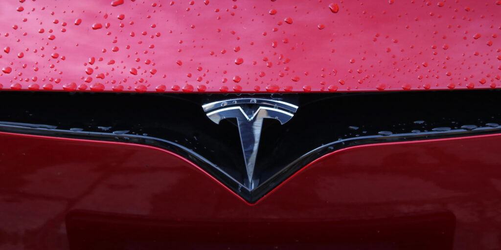 Detailaufnahme des Tesla-Logos an einer roten Motorhaube