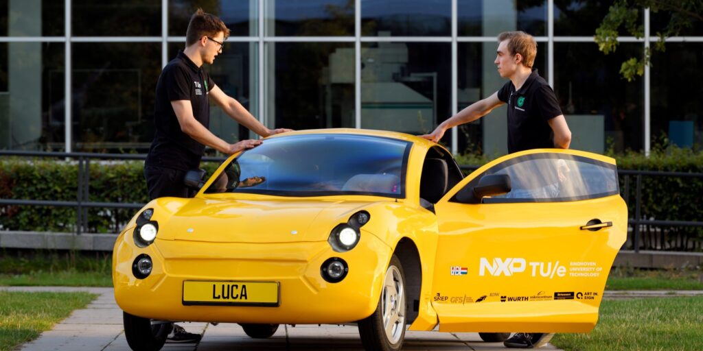 Zwei junge Männer stehen am gelben E-Auto Luca