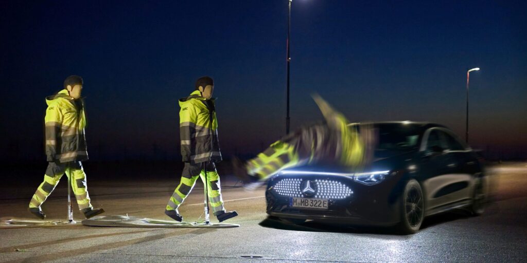 Dummies mit Warnwesten überqueren in der Dunkelheit eine Straße, während ein Auto sich nähert