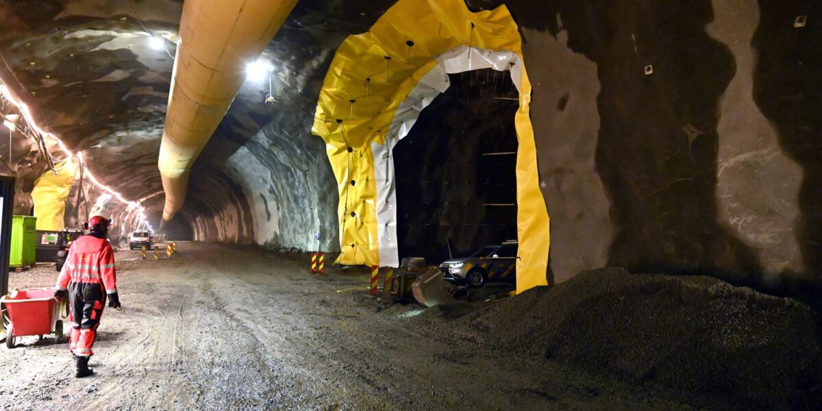 Beschäftigter in Warnkleidung im Rogfast-Tunnel; seitliche Öffnungen mit gelben und weißen Folien sowie eine Lüftungsleitung unter der Decke.