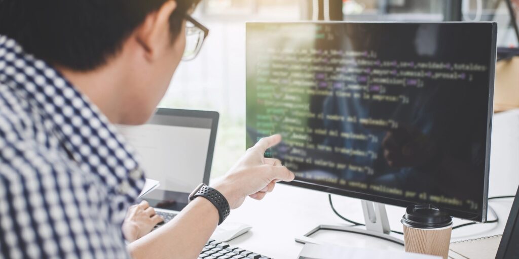 Ein Mann zeigt auf einen Computerbildschirm, auf dem Code zu sehen ist.