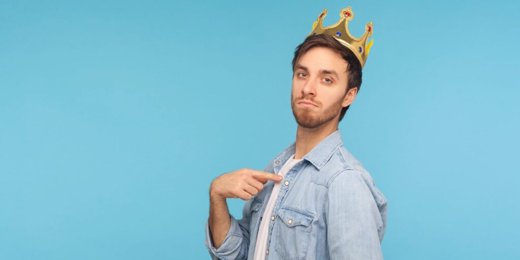 „Ich bin der König!“ Porträt eines ehrgeizigen Mannes mit goldener Krone, der auf sich selbst zeigt und arrogant in die Kamera blickt.