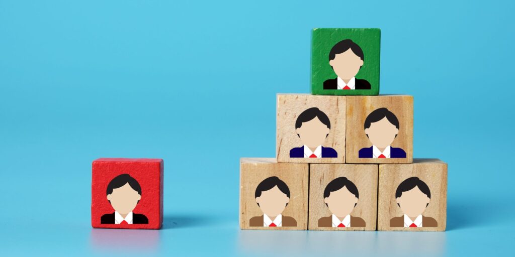 Symbolbild Führungskraft: Ein Bild von Holzklötzen mit Profil-Illustrationen. Unterschiedliche Hierarchieebenen sind durch verschiedene Farben gekennzeichnet. Konzept für Change Management und Organisation.