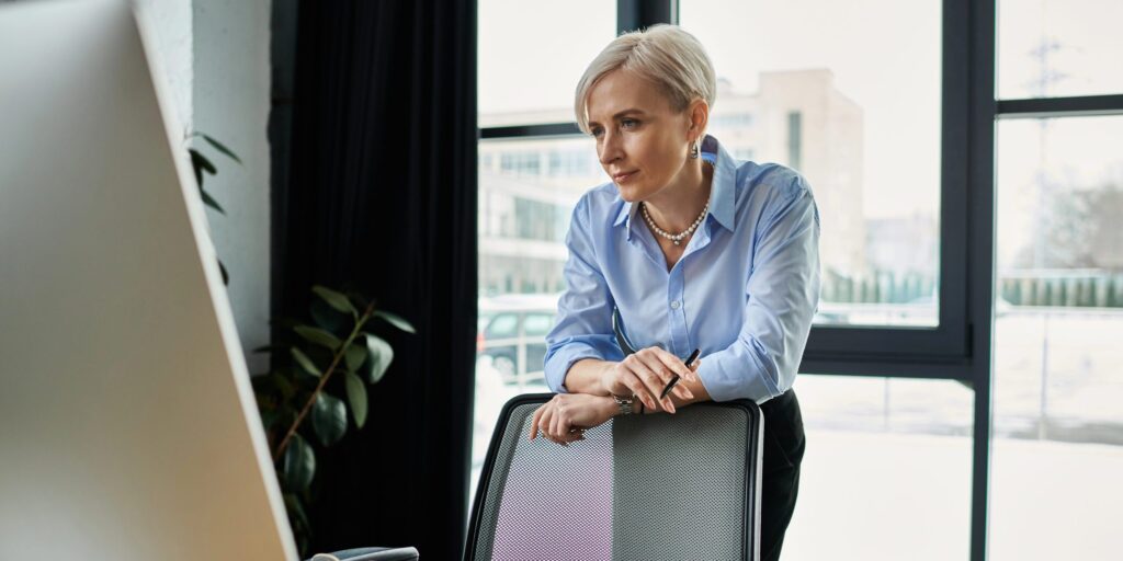 Frau lehnt an einem Bürostuhl und schaut auf einen Bildschirm
